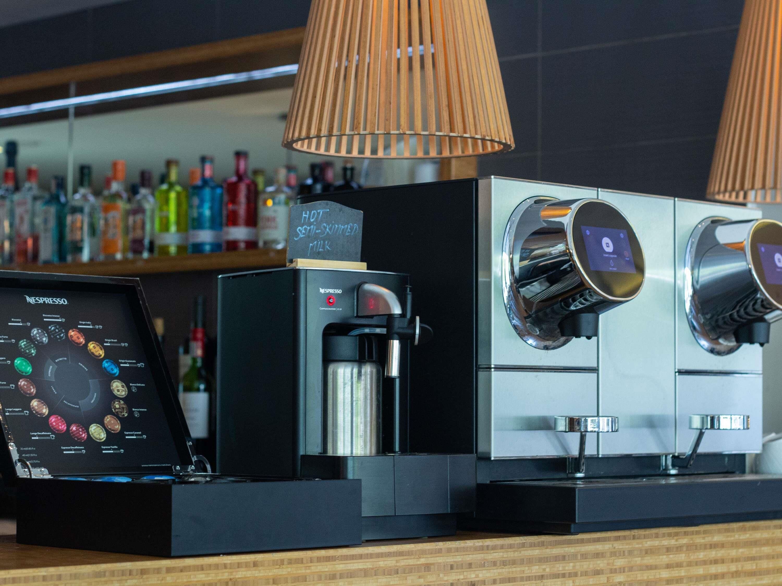 A coffee machine with a digital display, a milk frother, and a selection of coffee pods.