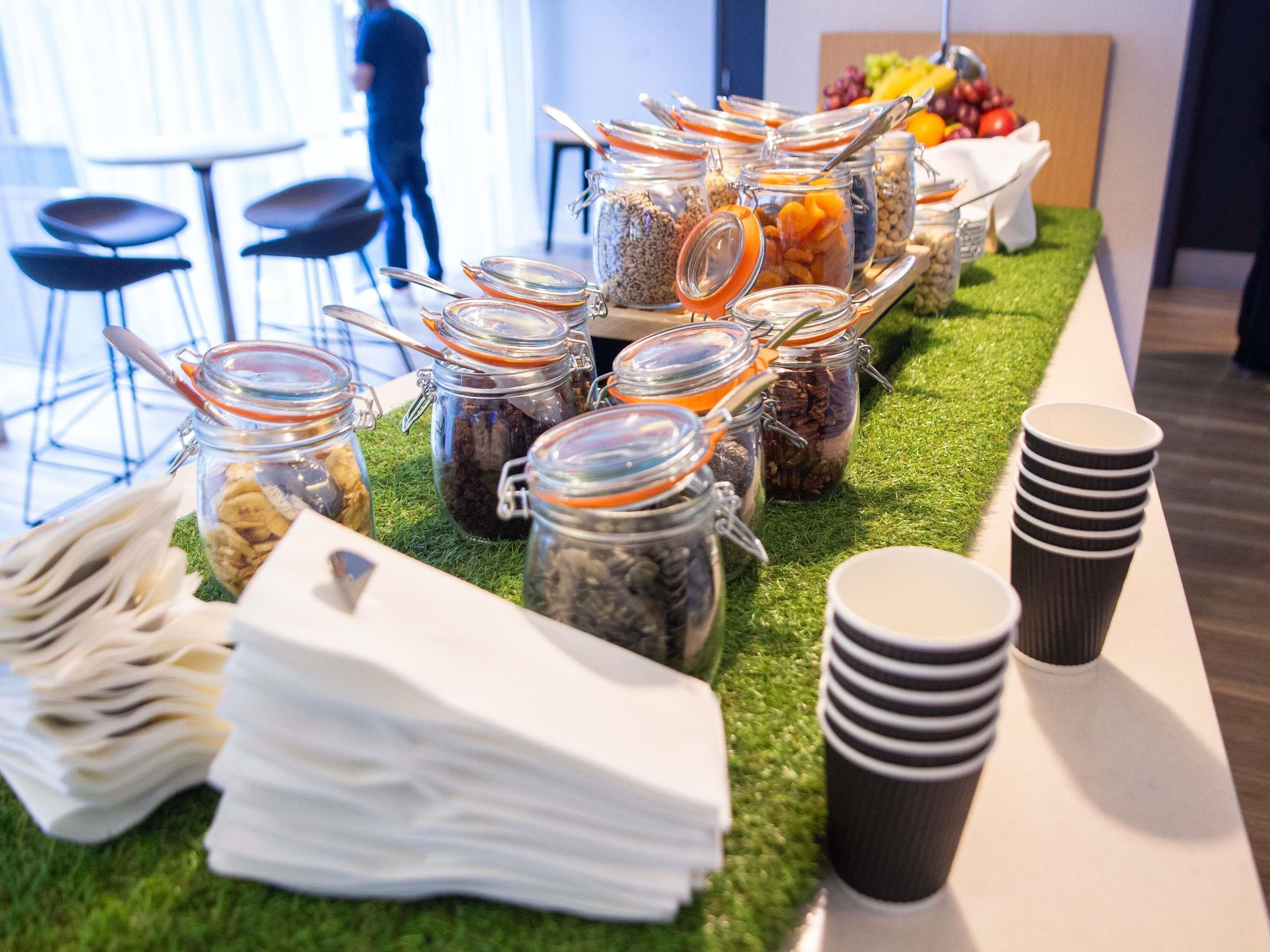 A buffet setup with food jars and disposable cups on a table.
