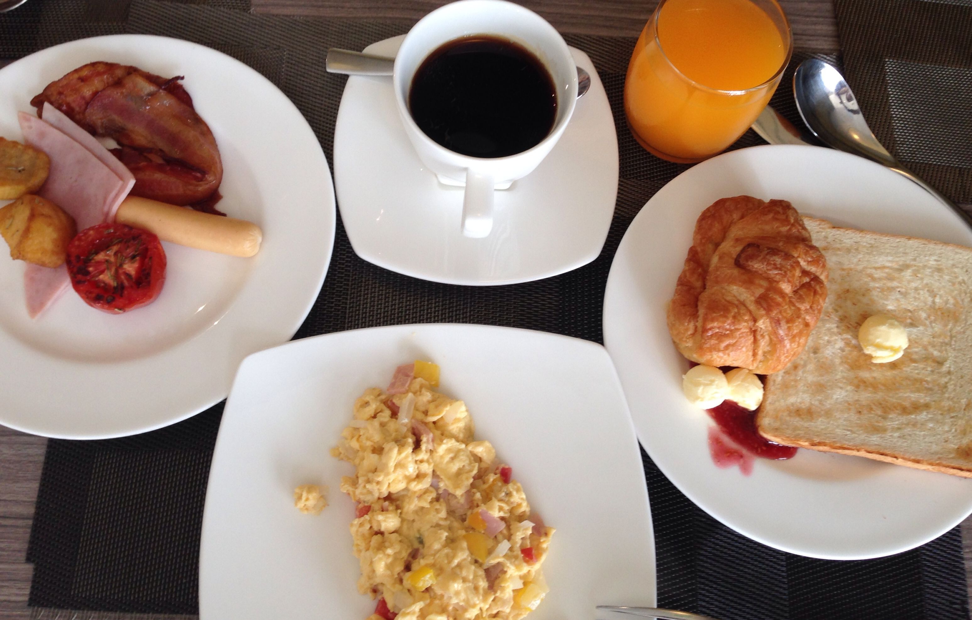 En morgenmadsborddækning med røræg, bacon, ristet brød og en kop kaffe.