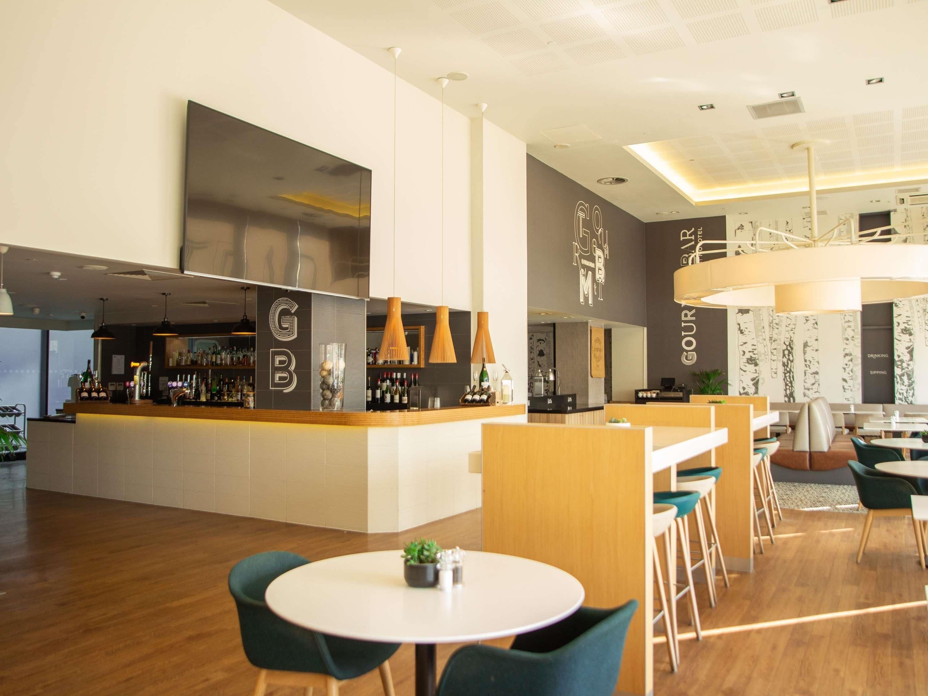 Una moderna area bar con un bancone, sgabelli da bar e una zona salotto con tavoli rotondi e sedie.