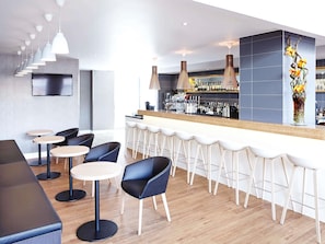 A modern bar area with multiple seating options, including bar stools and round tables, and a bar counter with a wine display. - Novotel London Wembley (Wembley)