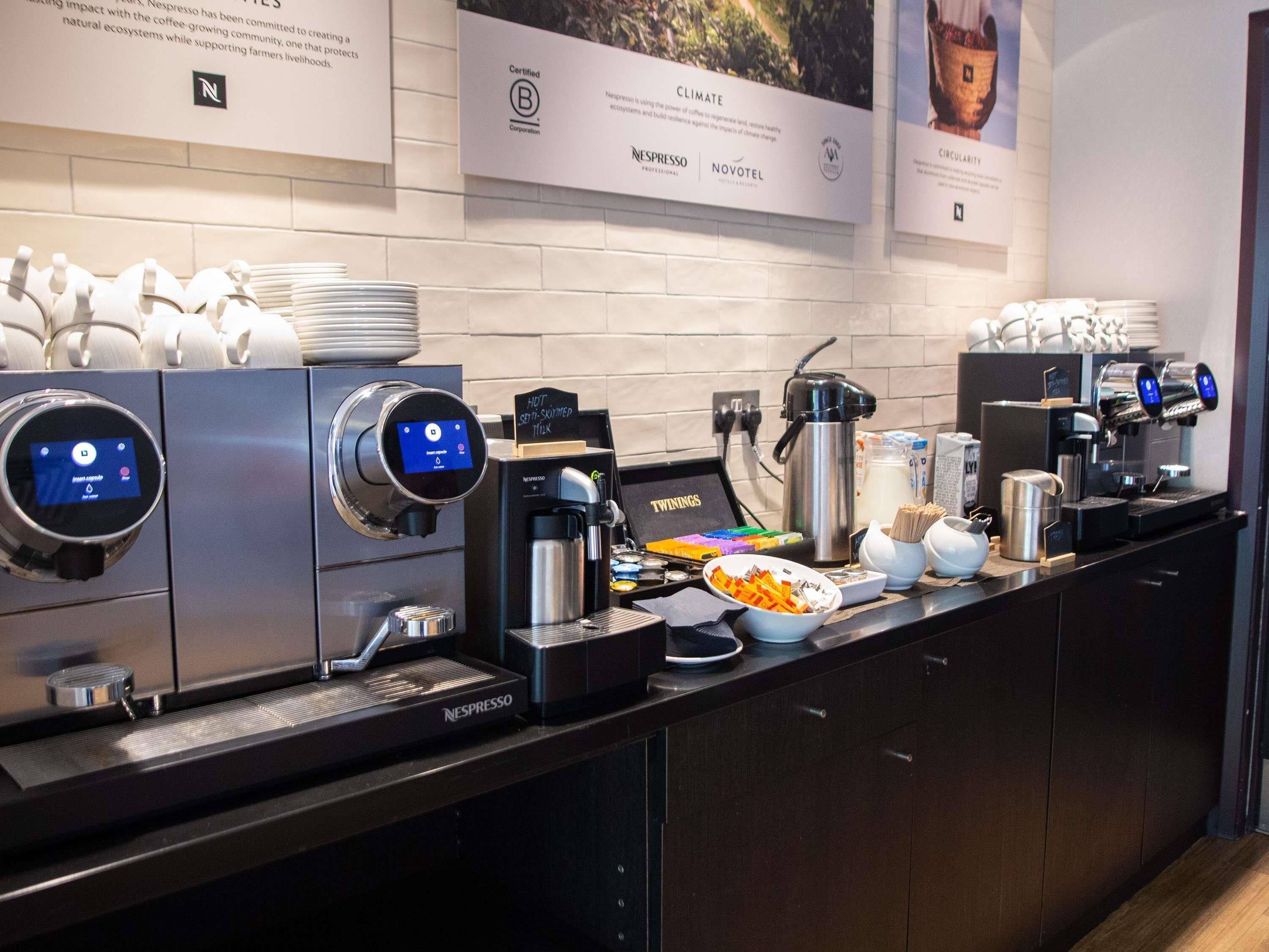 A coffee station with multiple Nespresso machines, a hot drink station, and a bowl of snacks.