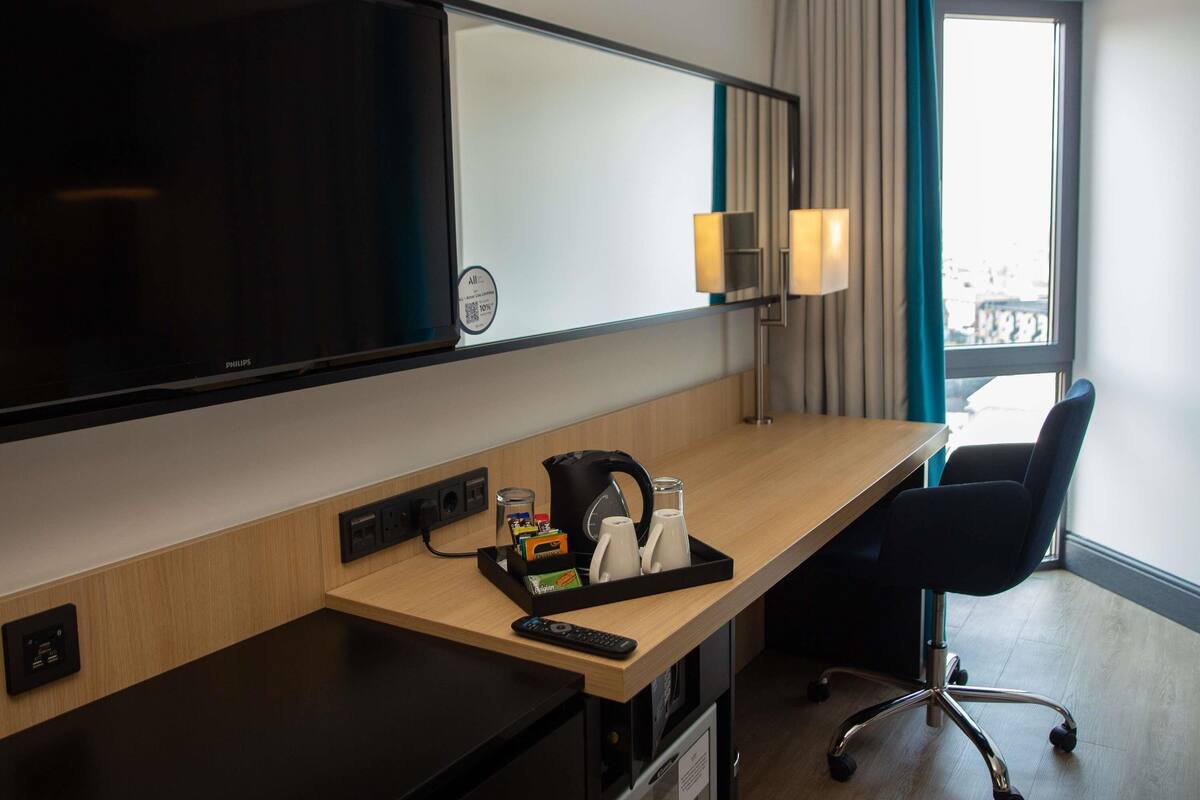 Une chambre d’hôtel équipée d’un téléviseur à écran plat, d’un bureau avec une machine à café, d’une télécommande et d’une chaise.