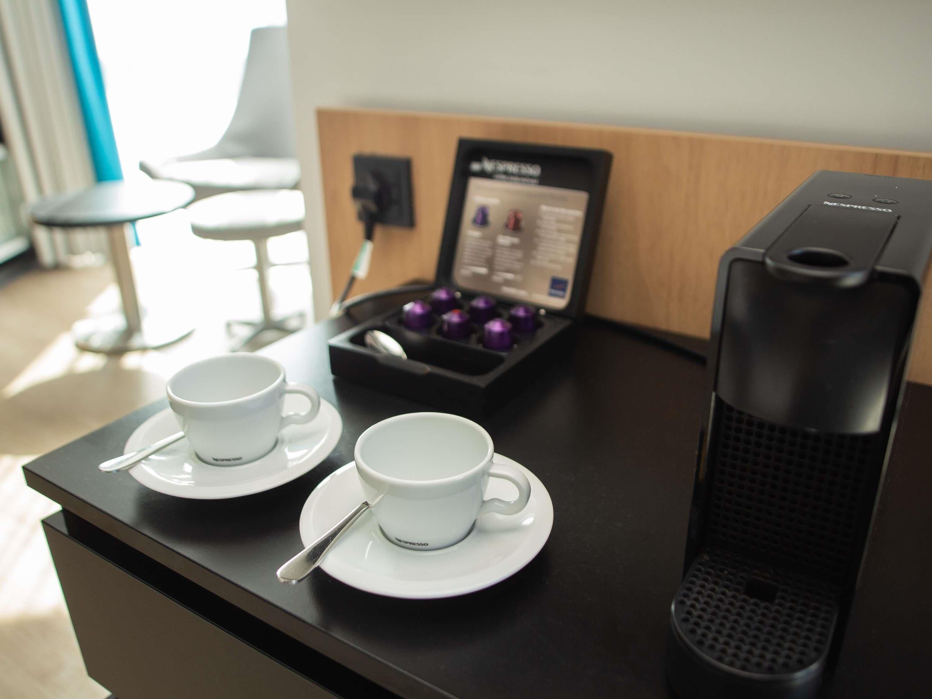 A coffee machine and two cups on a counter with a menu stand in the background.