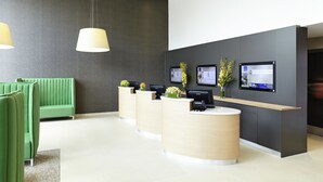 Un espace d’accueil avec un canapé vert, un comptoir d’accueil en bois et deux écrans fixés au mur.