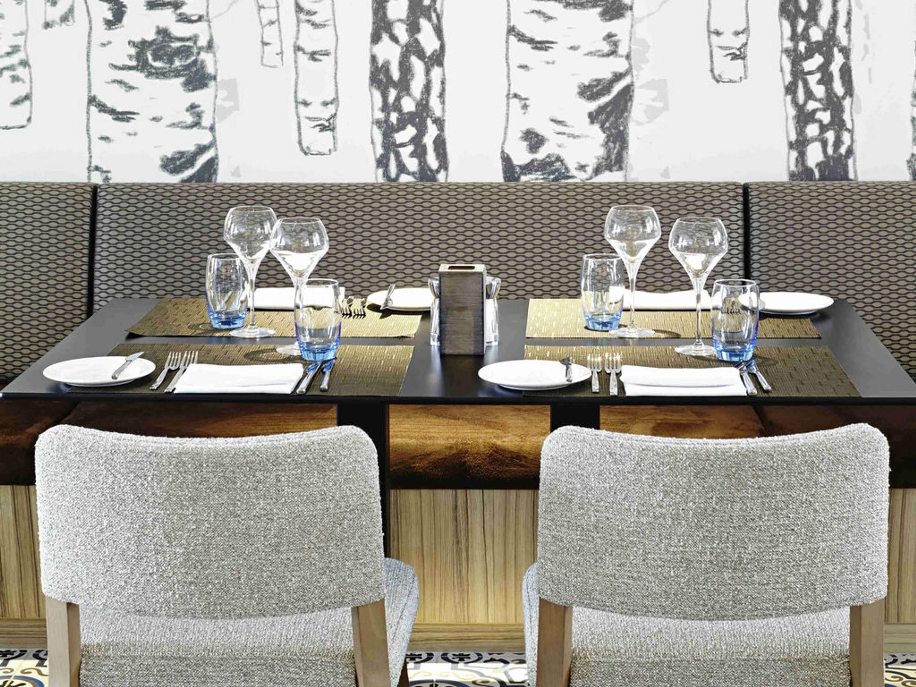 A dining table set with plates, cutlery, and glasses, with a patterned wall behind.