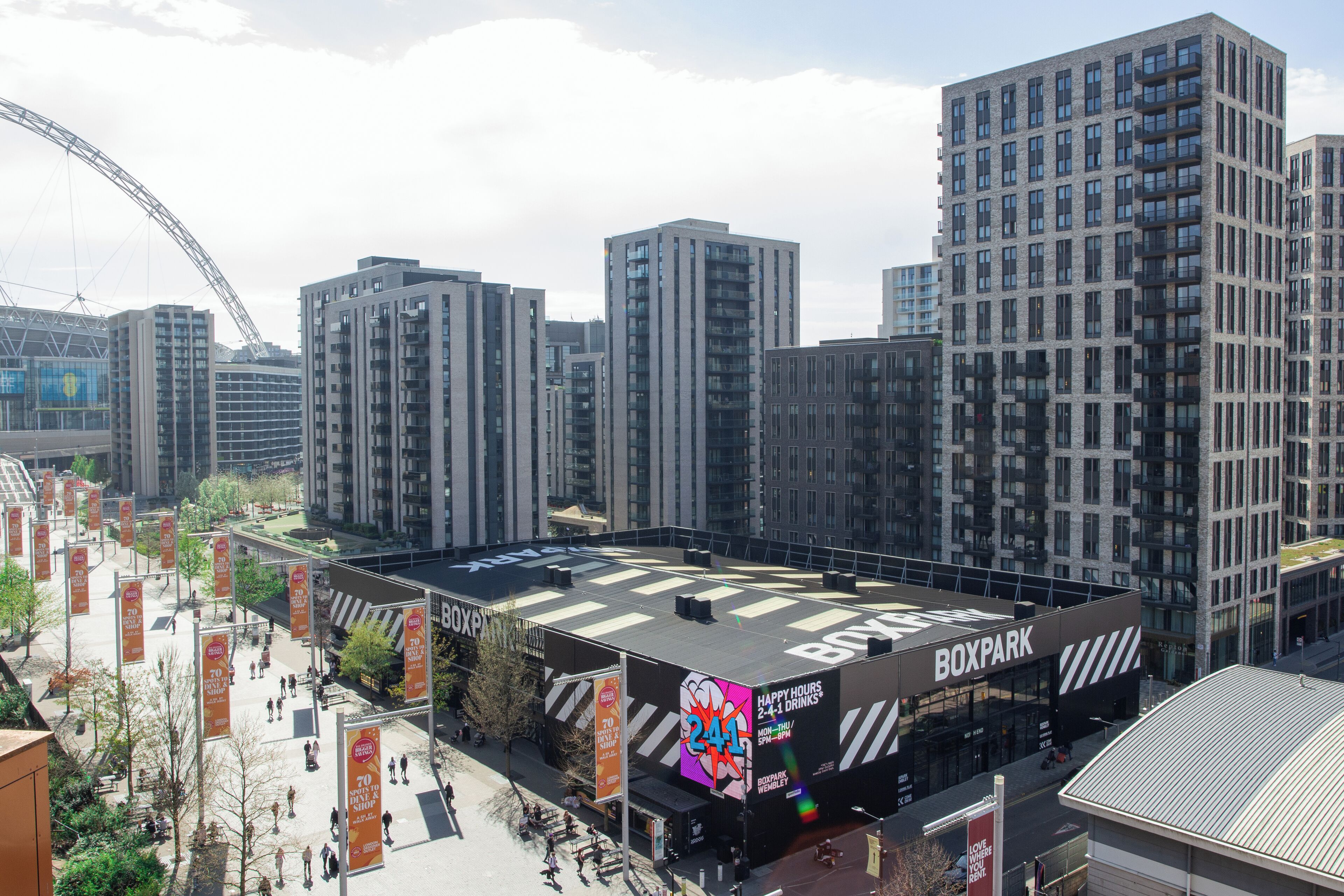 A modern building with a prominent 'Boxpark' sign, surrounded by high-rise buildings and a large arch structure in the background.