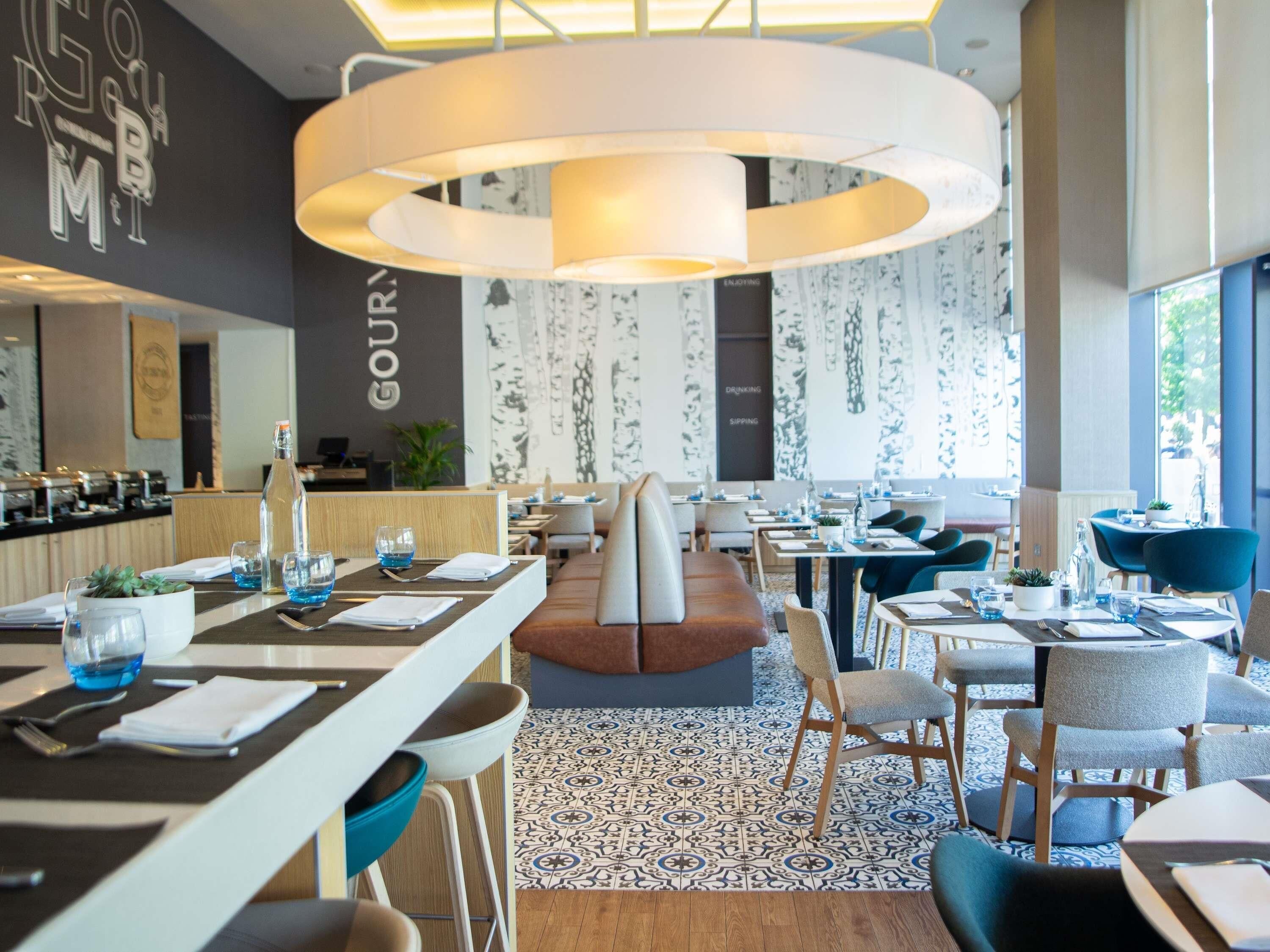 Un interior de restaurante moderno con una zona de estar central, varias mesas para comer y una lámpara circular grande.