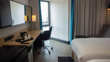 A hotel room with a bed, a desk with a chair, a TV, and a window with curtains.