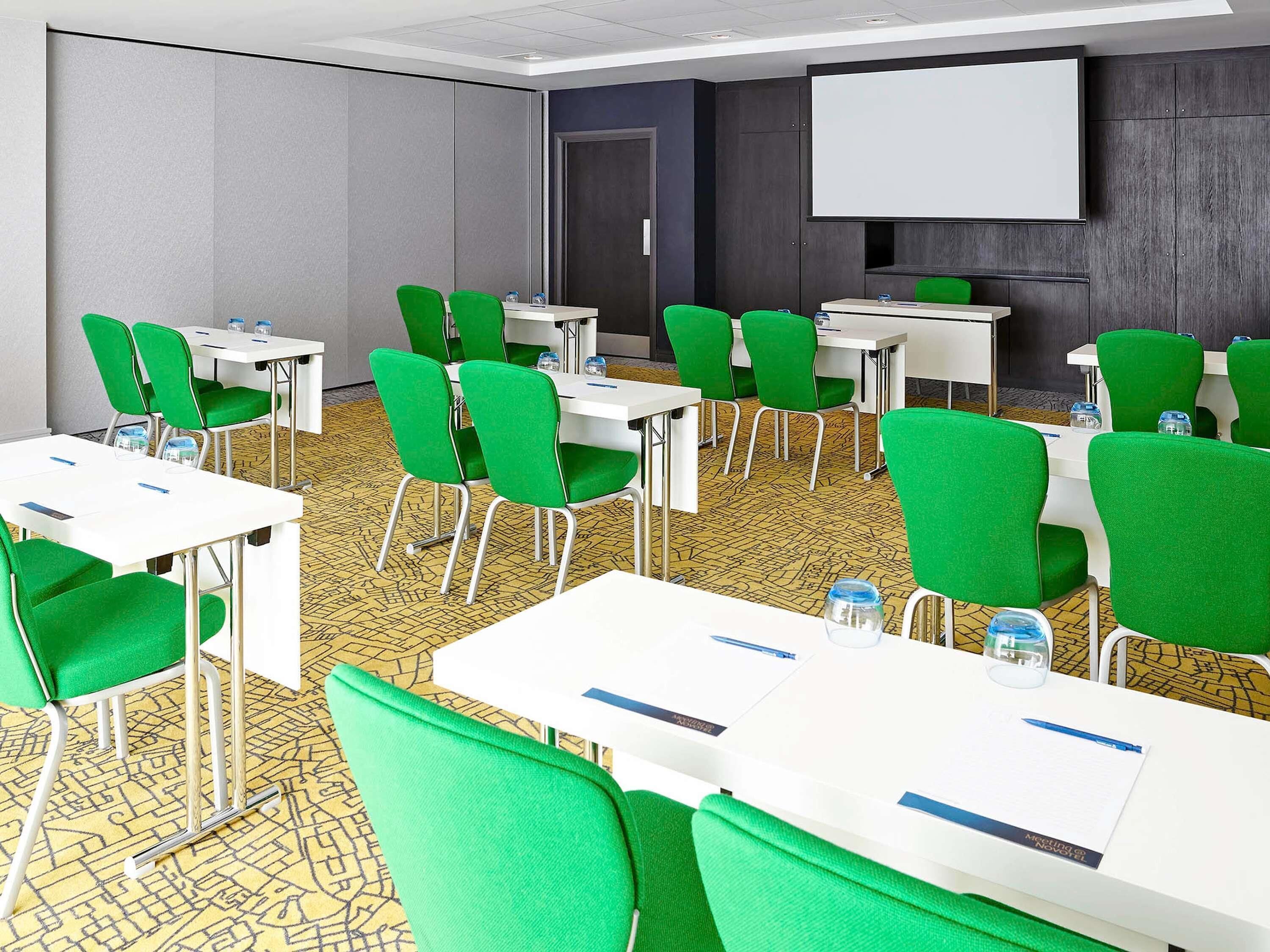 A conference room with green chairs, white tables, and a projector screen.
