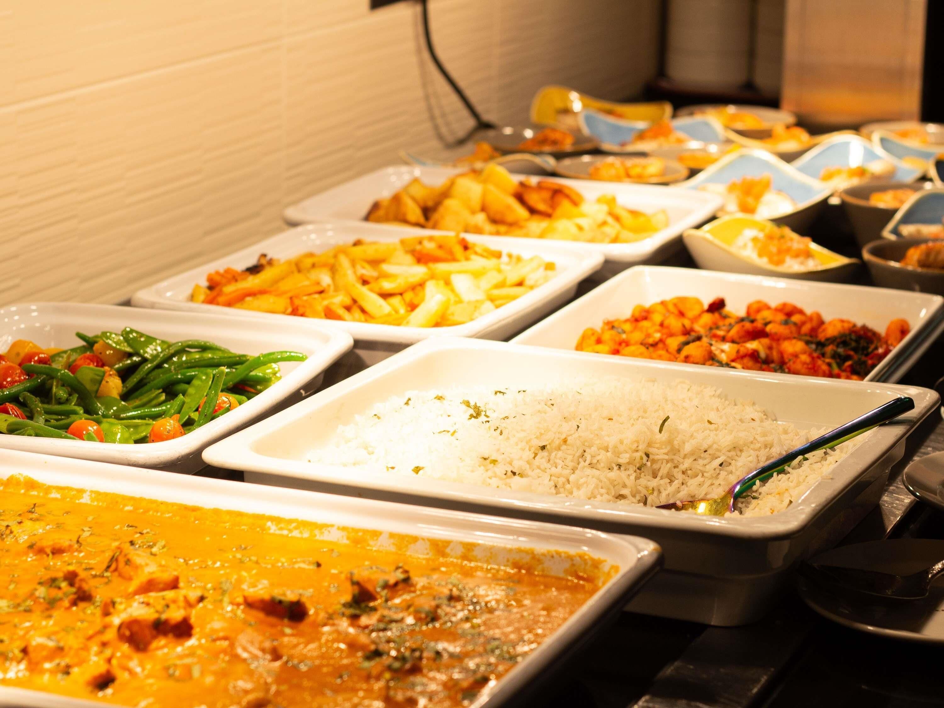 Buffet com diversos pratos, incluindo arroz, legumes e curry.
