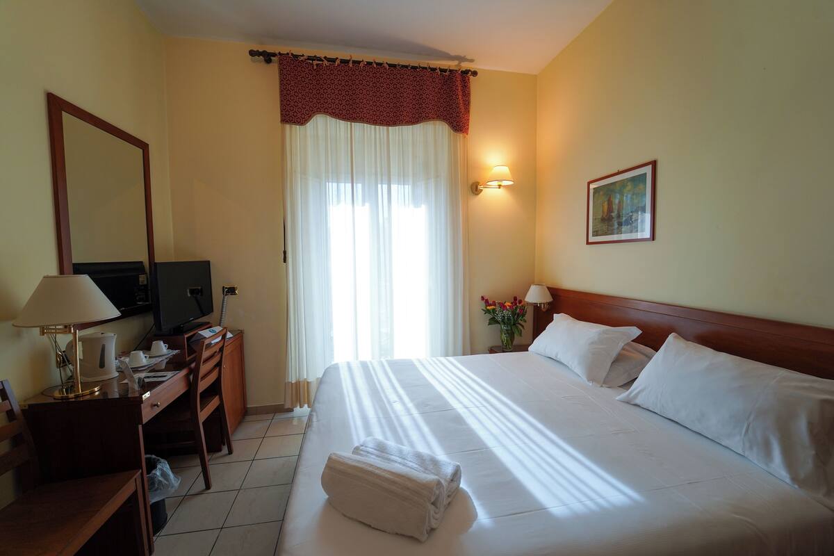 Una camera d'albergo con un letto, una scrivania con una lampada, una televisione e un quadro appeso al muro.