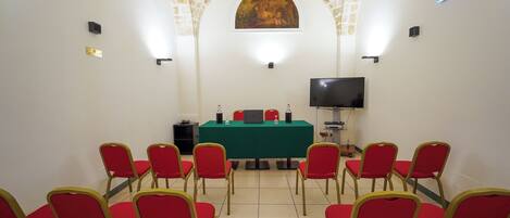 A conference room with a green table, red chairs, a TV, and a painting on the wall.