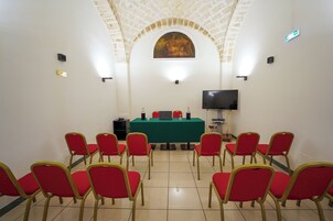 Una sala de conferencias con una mesa verde, sillas rojas, un televisor y un cuadro en la pared.