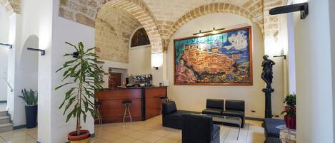 A lobby with a high ceiling, stone arches, a large mural, seating area, and a coffee bar.