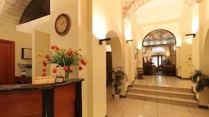 A hotel reception area with a reception desk, a clock, and a staircase leading to the upper floor. - Hotel Adria (Bari)