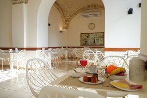 A breakfast setting with white chairs, a table with breakfast items, and a clock on the wall. - Hotel Adria (Bari)