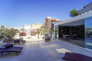 A rooftop terrace with lounge chairs, a dining area, and a glass wall offering a city view. - Hotel Adria (Bari)