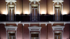 A building facade with three symmetrical windows, each framed by ornate moldings and illuminated by exterior lighting. - Hotel Adria (Bari)