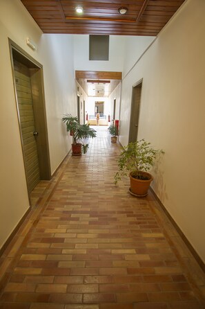 Un pasillo con suelo de baldosas, plantas en macetas y puertas que dan a habitaciones.