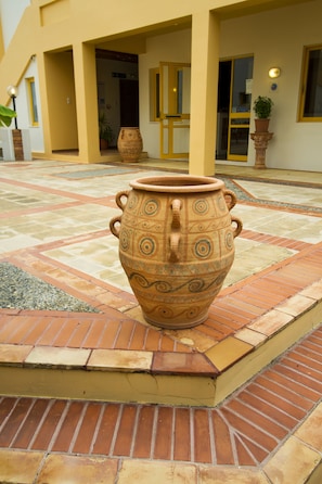 Una maceta grande de terracota en un patio con suelo de baldosas y paredes amarillas.