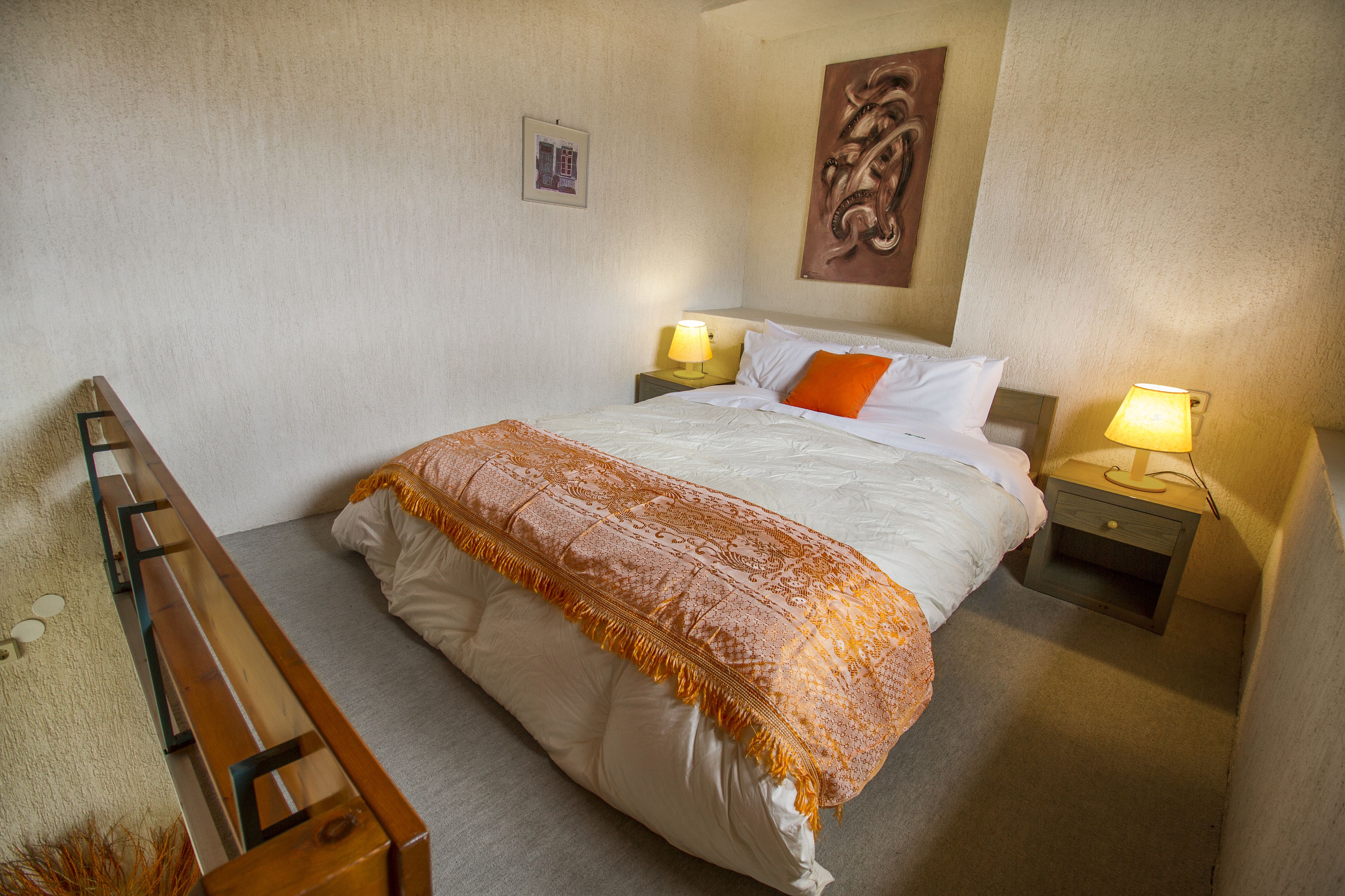 A neatly made bed with a patterned blanket, two bedside lamps, and a wall-mounted artwork.