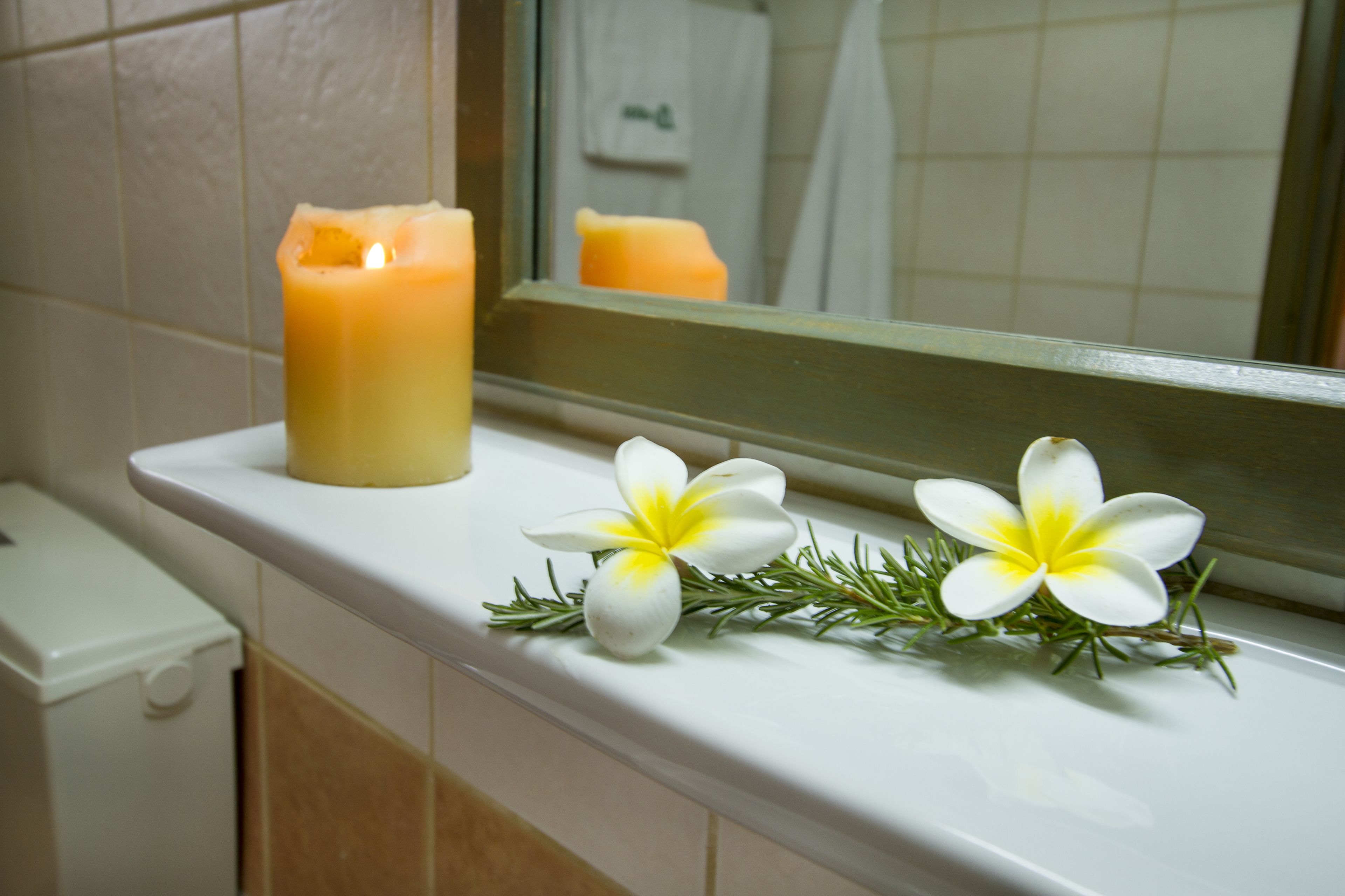 Un baño con encimera blanca, una vela encendida y dos flores blancas con centros amarillos.