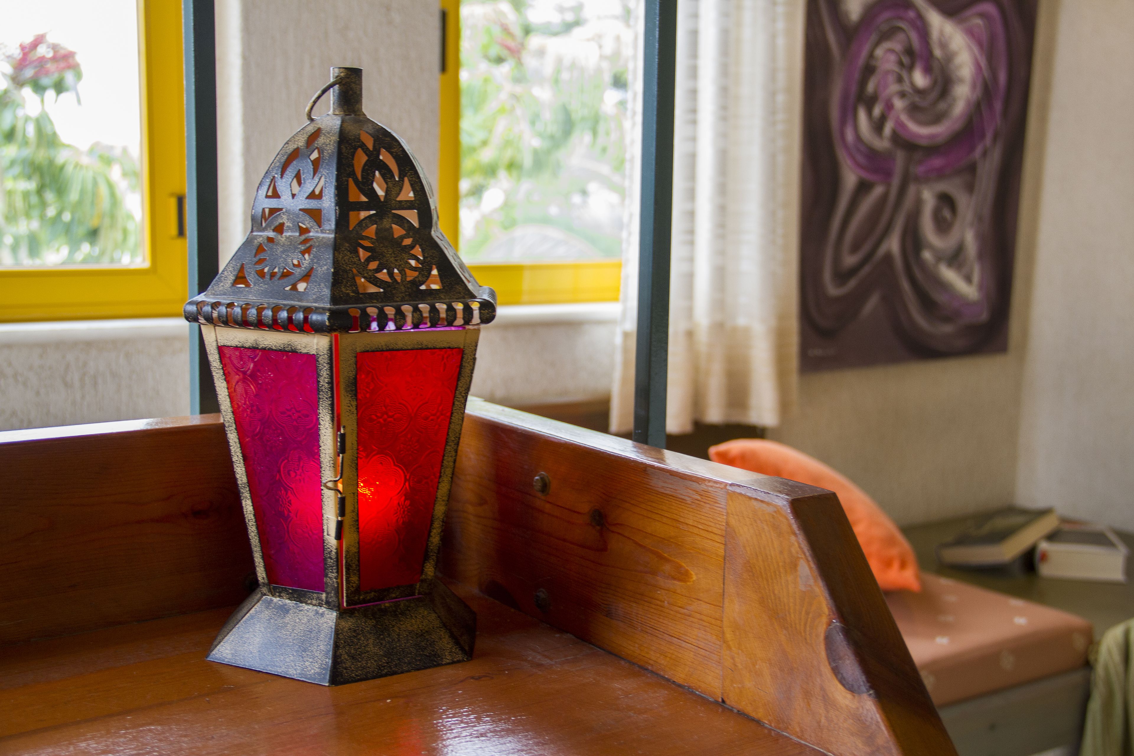 A wooden bench with a decorative metal lantern in front of a window with yellow frames.