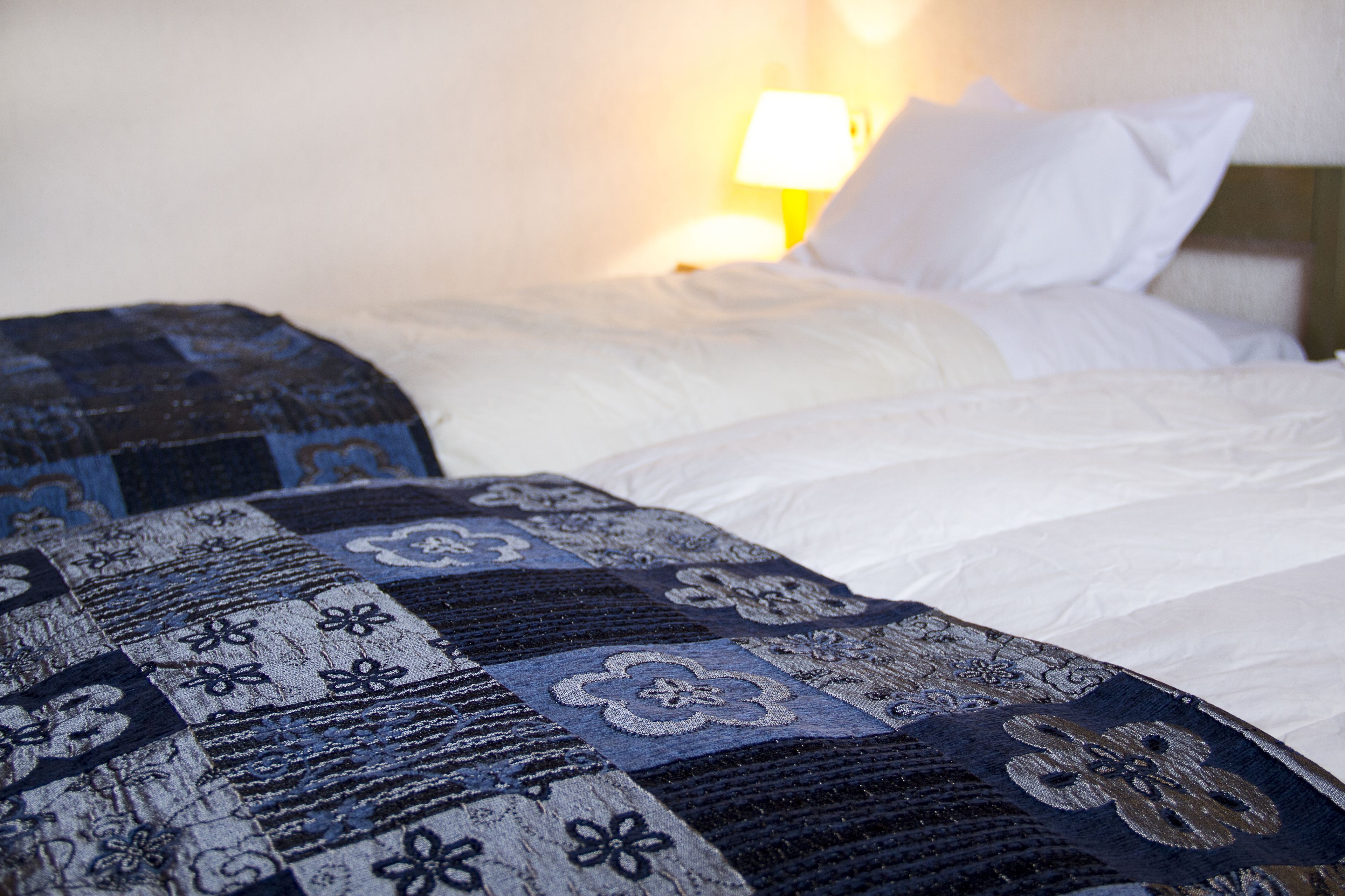 A hotel room with a neatly made bed, a patterned blanket, and a bedside lamp.