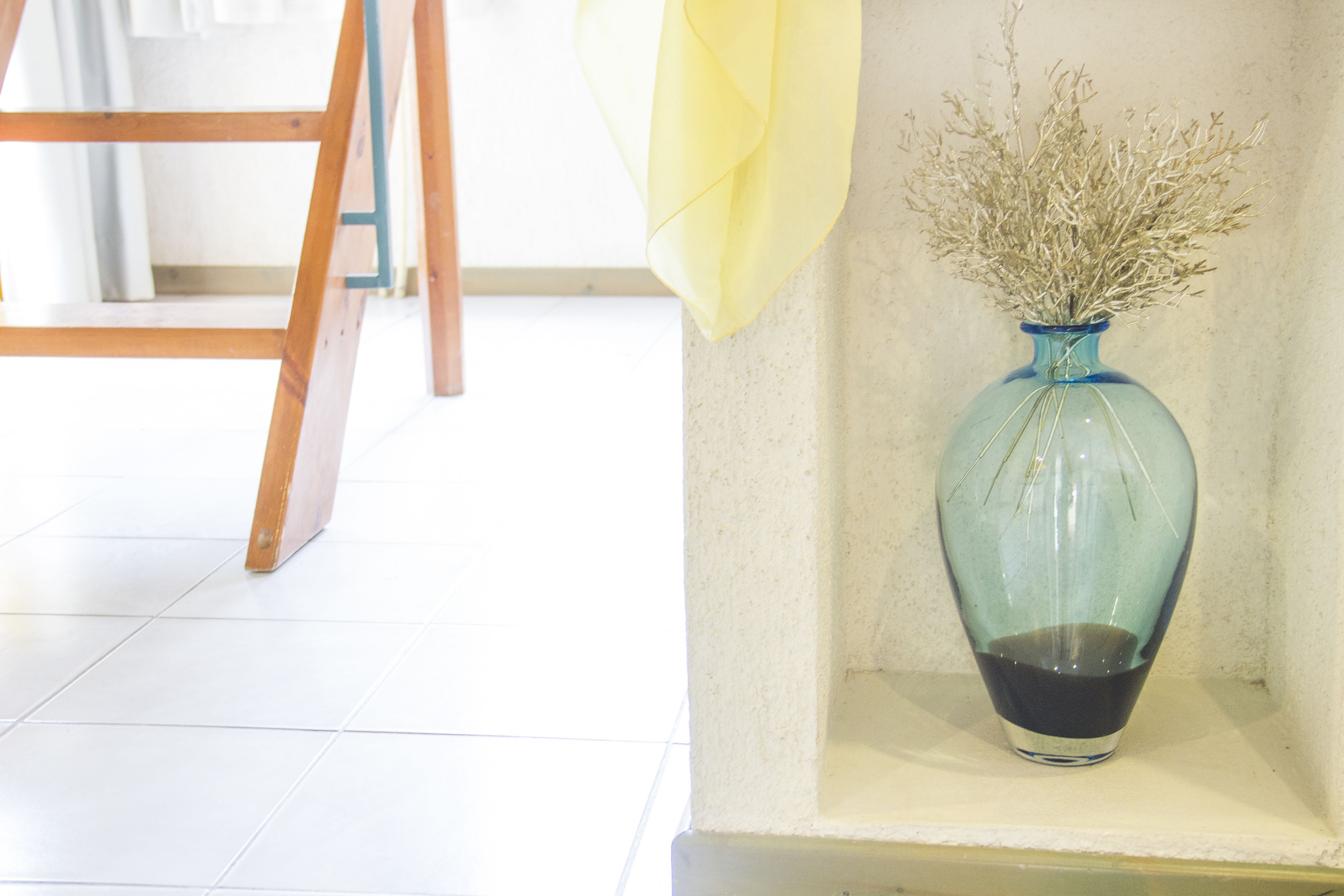 A blue vase with dried plants on a shelf.