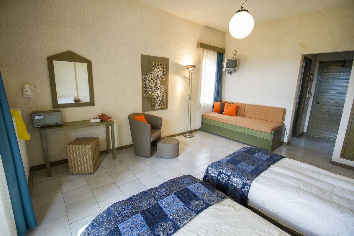 Ein Hotelzimmer mit zwei Betten, einem Schlafsofa, einem Schreibtisch mit Stuhl, einer Lampe und einem Fernseher.
