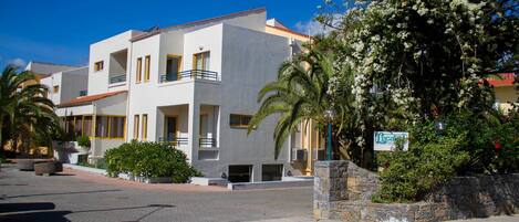 A modern two-story building with balconies, a paved driveway, and a stone wall with a sign.