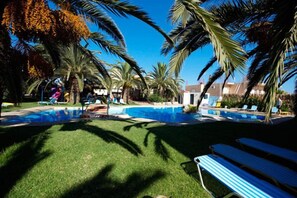 Piscina rodeada por palmeiras e cadeiras de praia.
