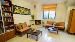 A living room with two sofas, a coffee table, a fireplace, a bookshelf, and a painting on the wall. - Lycasti Maisonettes (Platanias)