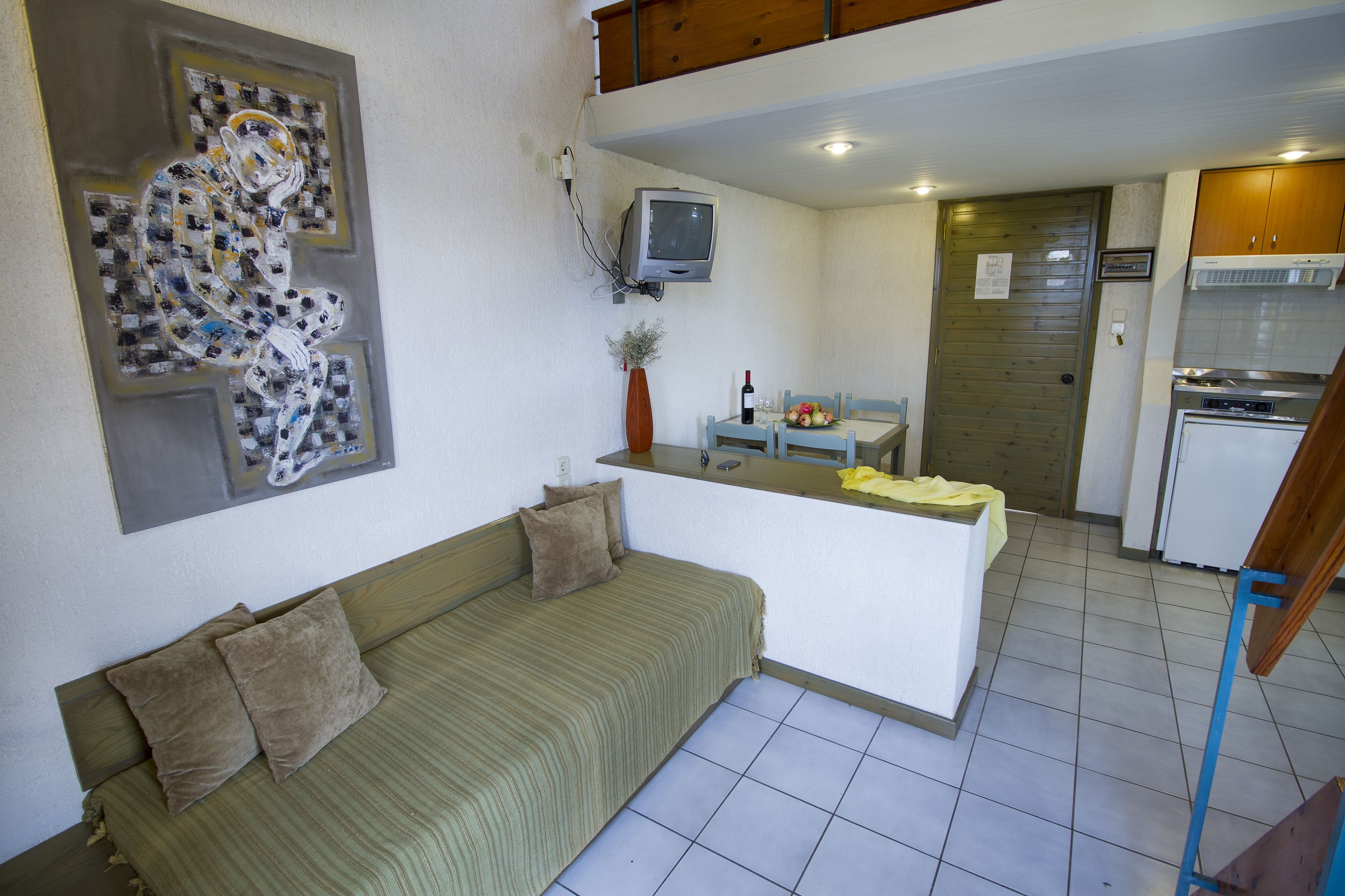 Un espacio habitable compacto con sofá, una pequeña mesa de comedor, televisión y kitchenette.