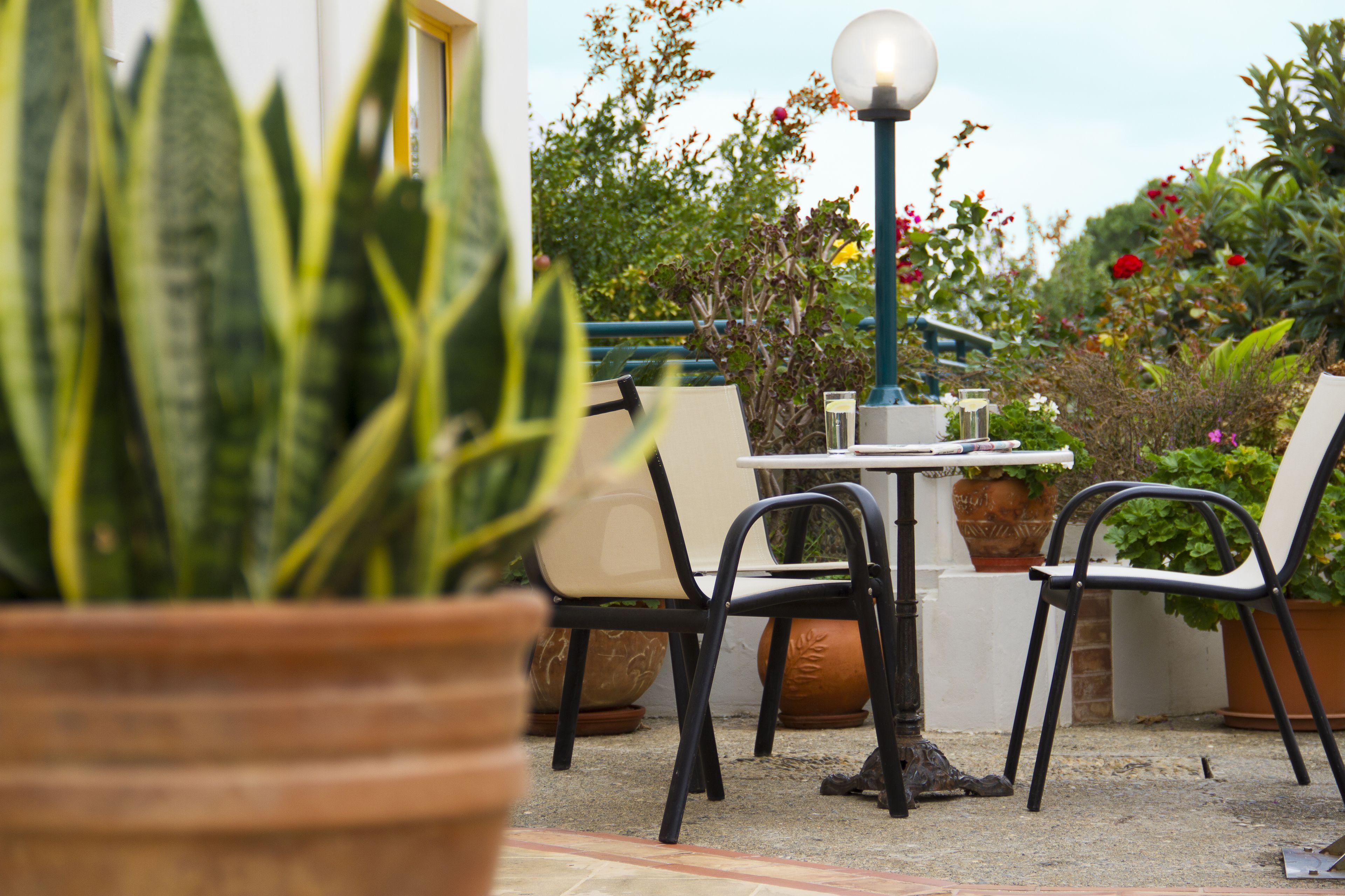 Een terras met een ronde tafel, twee stoelen, plantenpotten en een lantaarn.