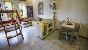 A living room with a sofa, a coffee table, a TV mounted on the wall, and a dining area with a table and chairs. - Lycasti Maisonettes (Platanias)