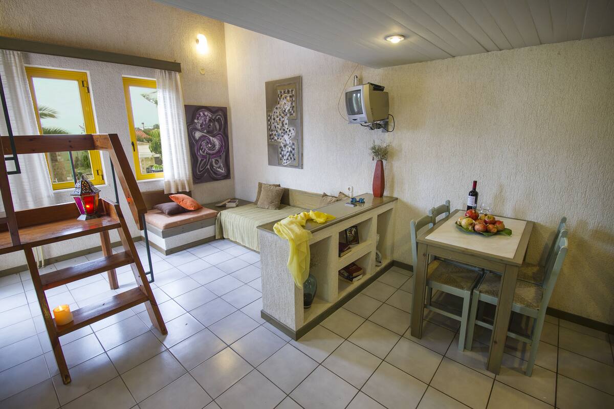 Ein Wohnzimmer mit einer Couch, einem Couchtisch, einem an der Wand befestigten Fernseher und einem Essbereich mit Tisch und Stühlen.