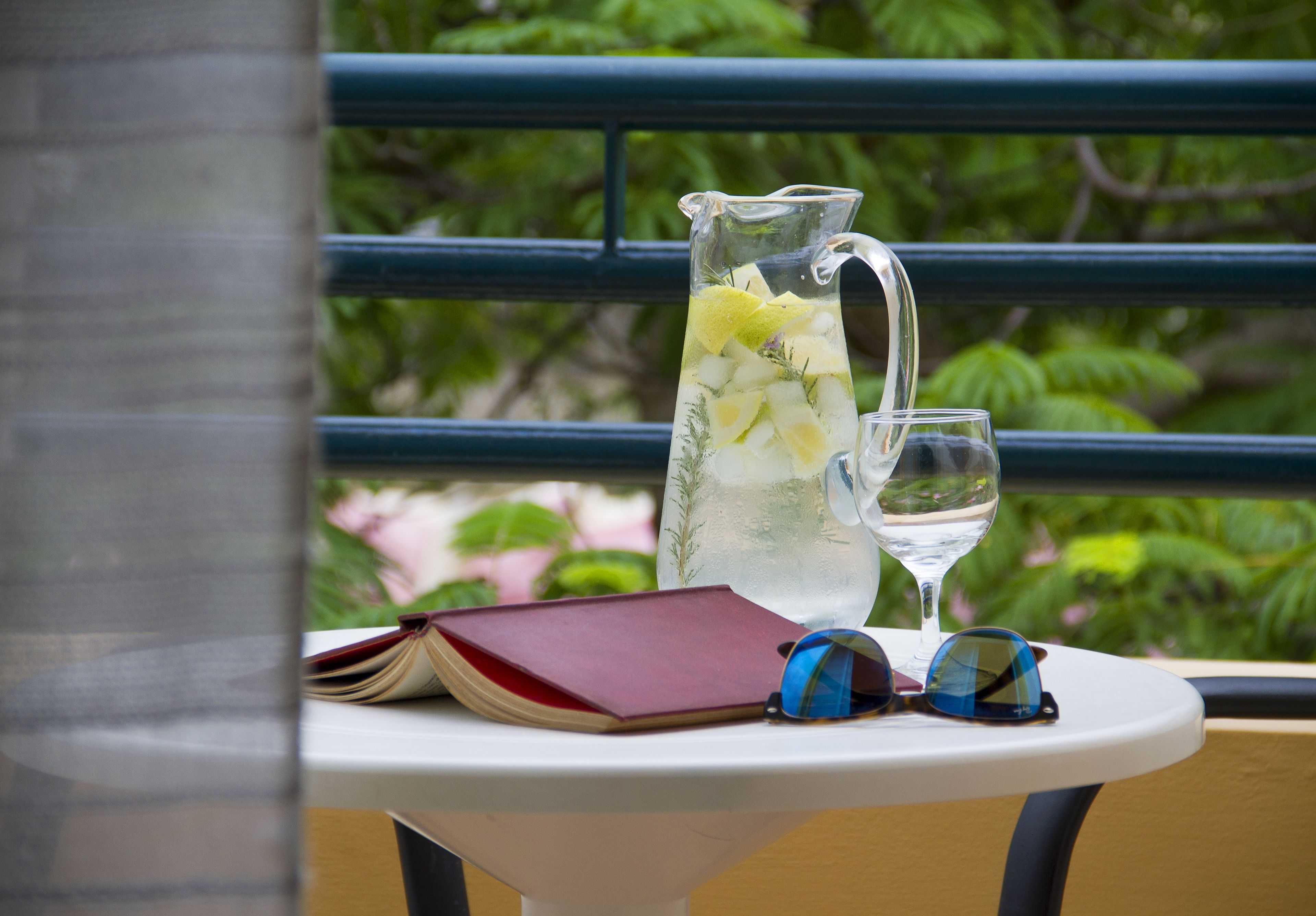 A table with a pitcher of iced tea, a glass of water, a book, and a pair of sunglasses.