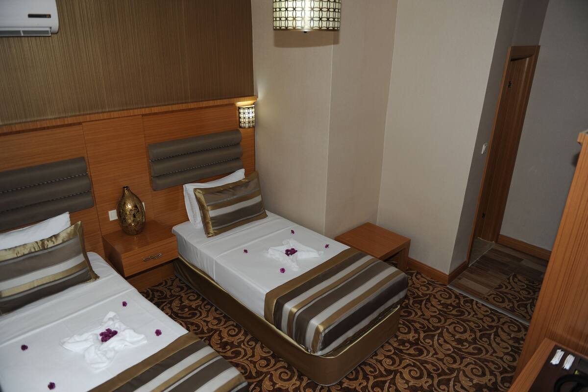 A hotel room with two beds, a wooden headboard, a bedside table with a lamp, and a patterned carpet.