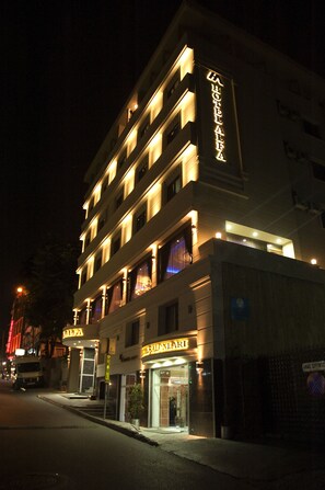A multi-story hotel with illuminated signage, a ground-level entrance, and a visible parking area. - Alfa Hotel (Istanbul)