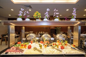 Un buffet proposant une variété d’aliments, notamment des fruits, des légumes et des fromages, présentés sur des assiettes et dans des bols.