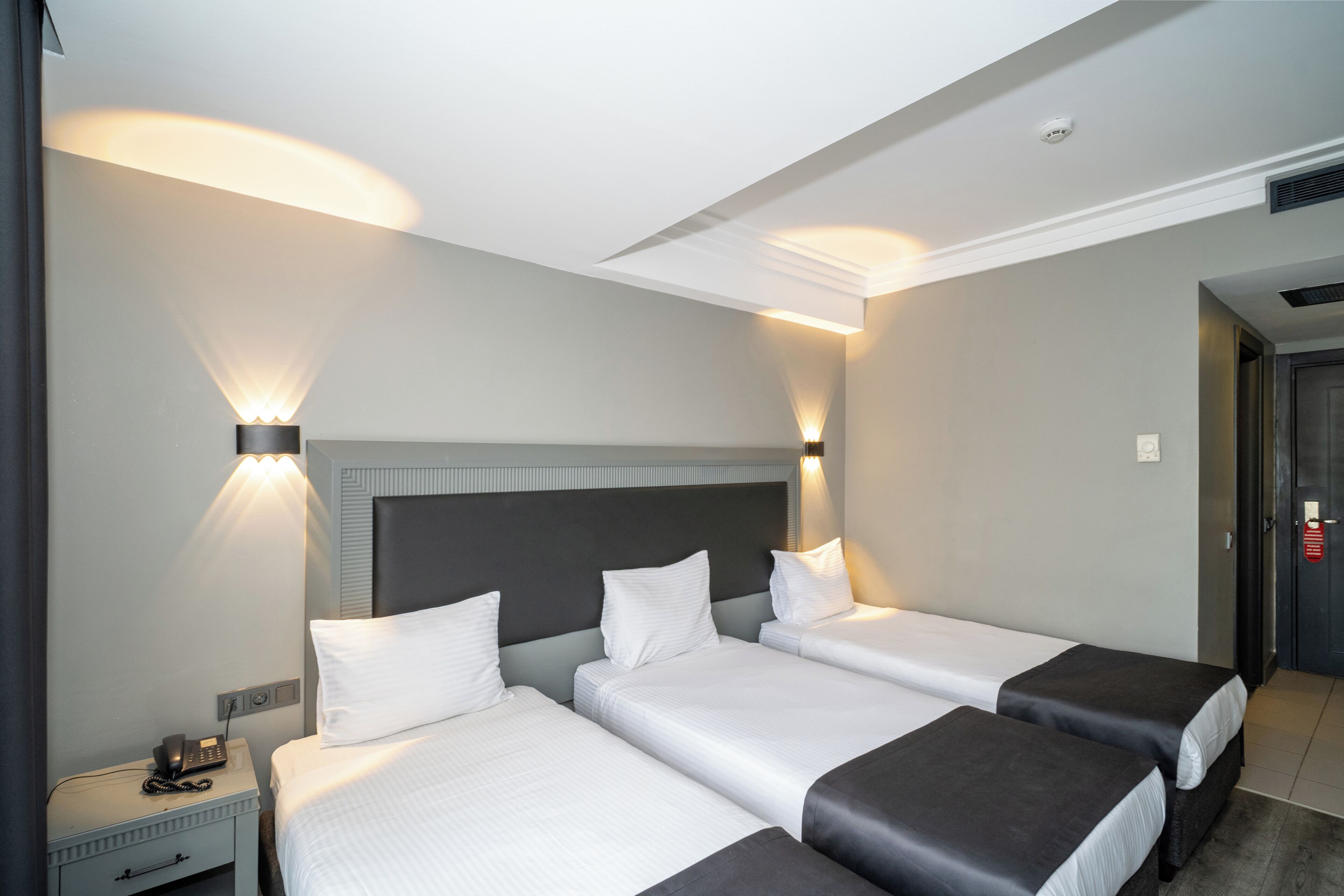 Habitación de hotel con tres camas, una mesita de noche con teléfono e iluminación empotrada.