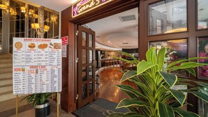 L'ingresso di un ristorante con un neon, una lavagna dei menù e una pianta in primo piano.