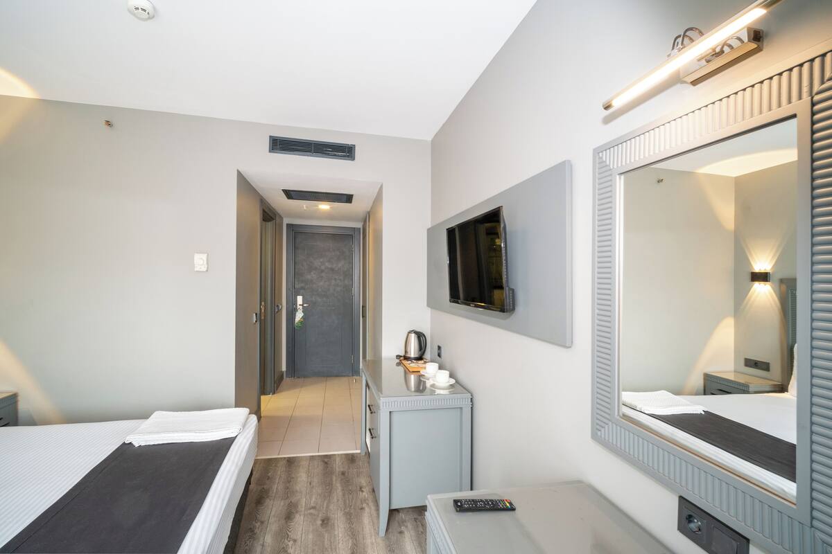 Ein Hotelzimmer mit Bett, Schreibtisch, Spiegel und einer Tür zu einem Flur.