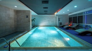 Una piscina con pavimento piastrellato, scaletta e sedie a sdraio lungo il bordo.