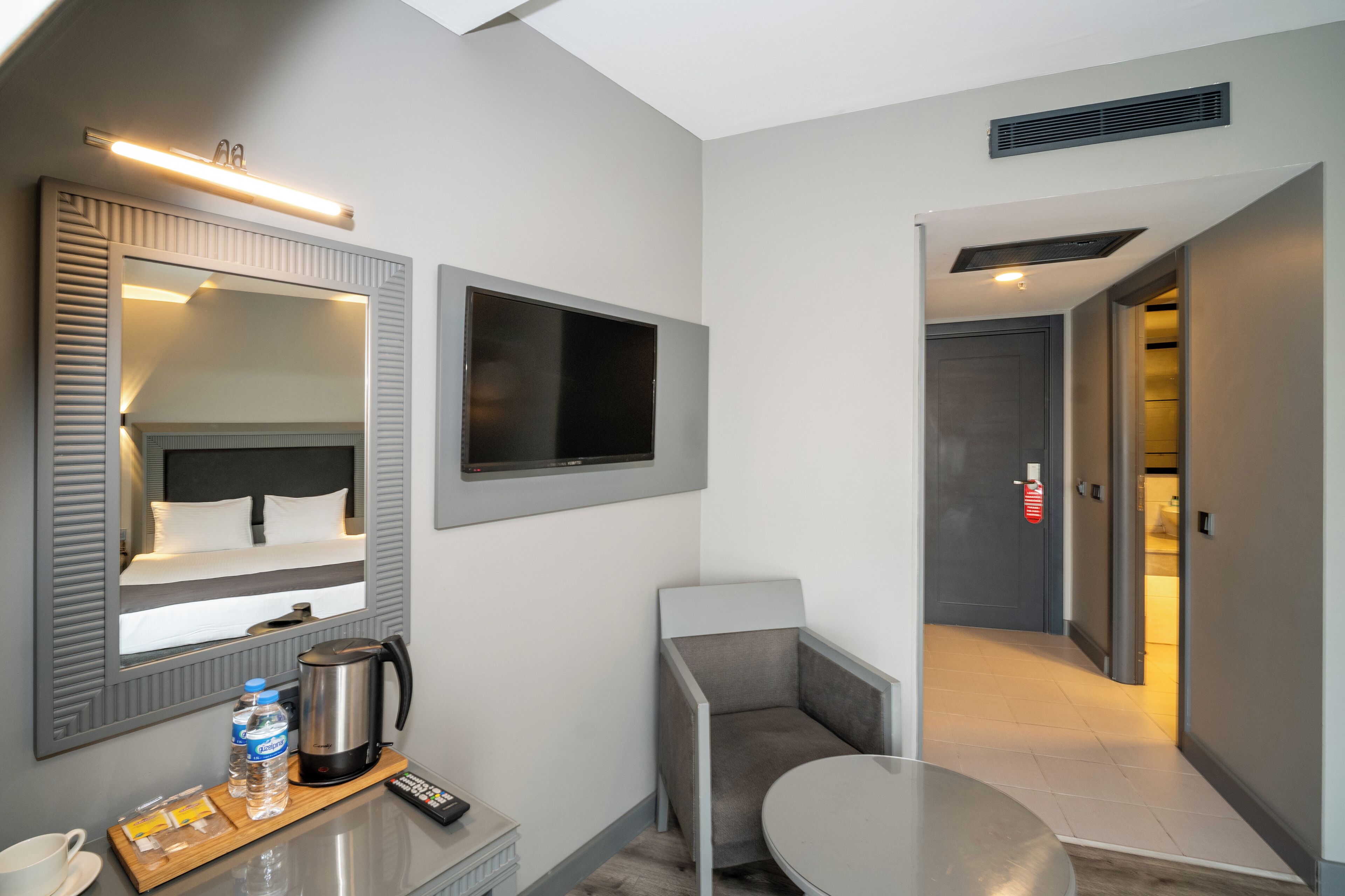 A hotel room with a bed, a TV, a coffee maker, a remote control, and a small table with a cup and a bottle.