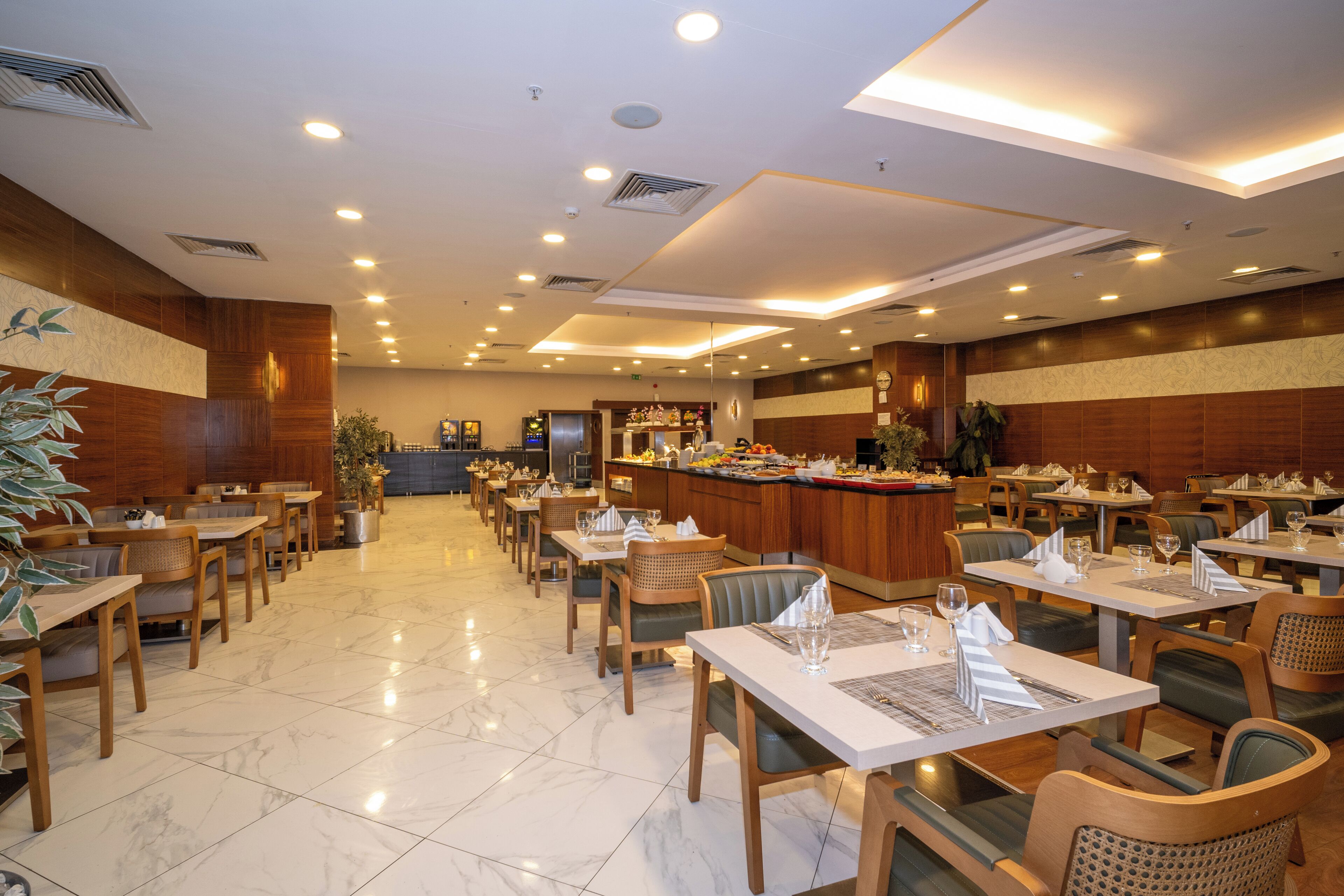A spacious restaurant with multiple dining tables and chairs, a central bar area, and a clean, well-lit interior.