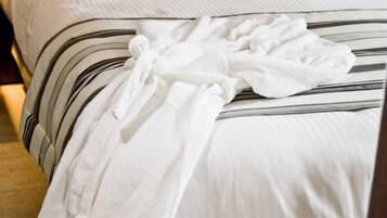 A neatly made bed with striped bedding and a white bathrobe draped over it.