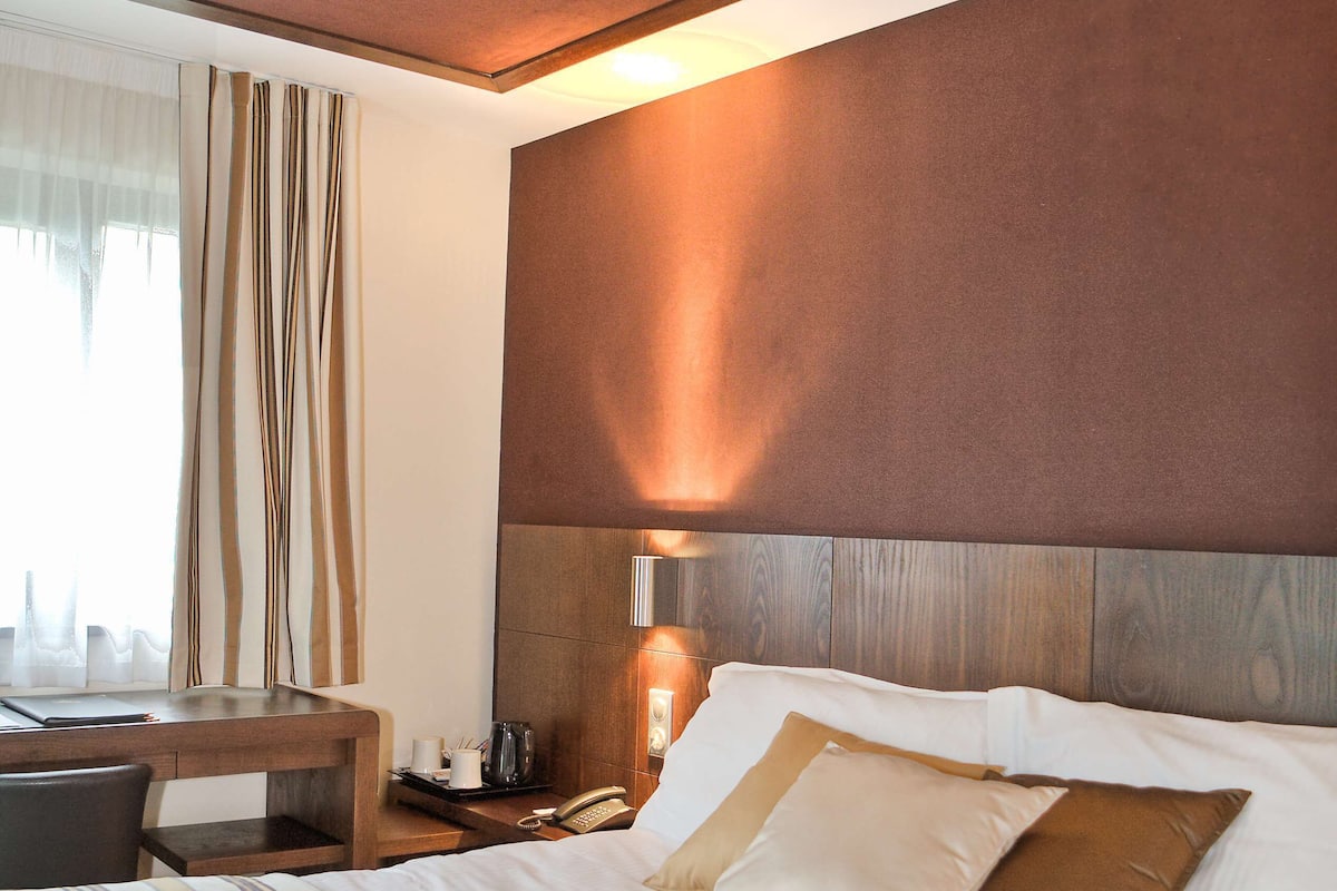 A hotel room with a large bed, a desk, and a window with curtains.